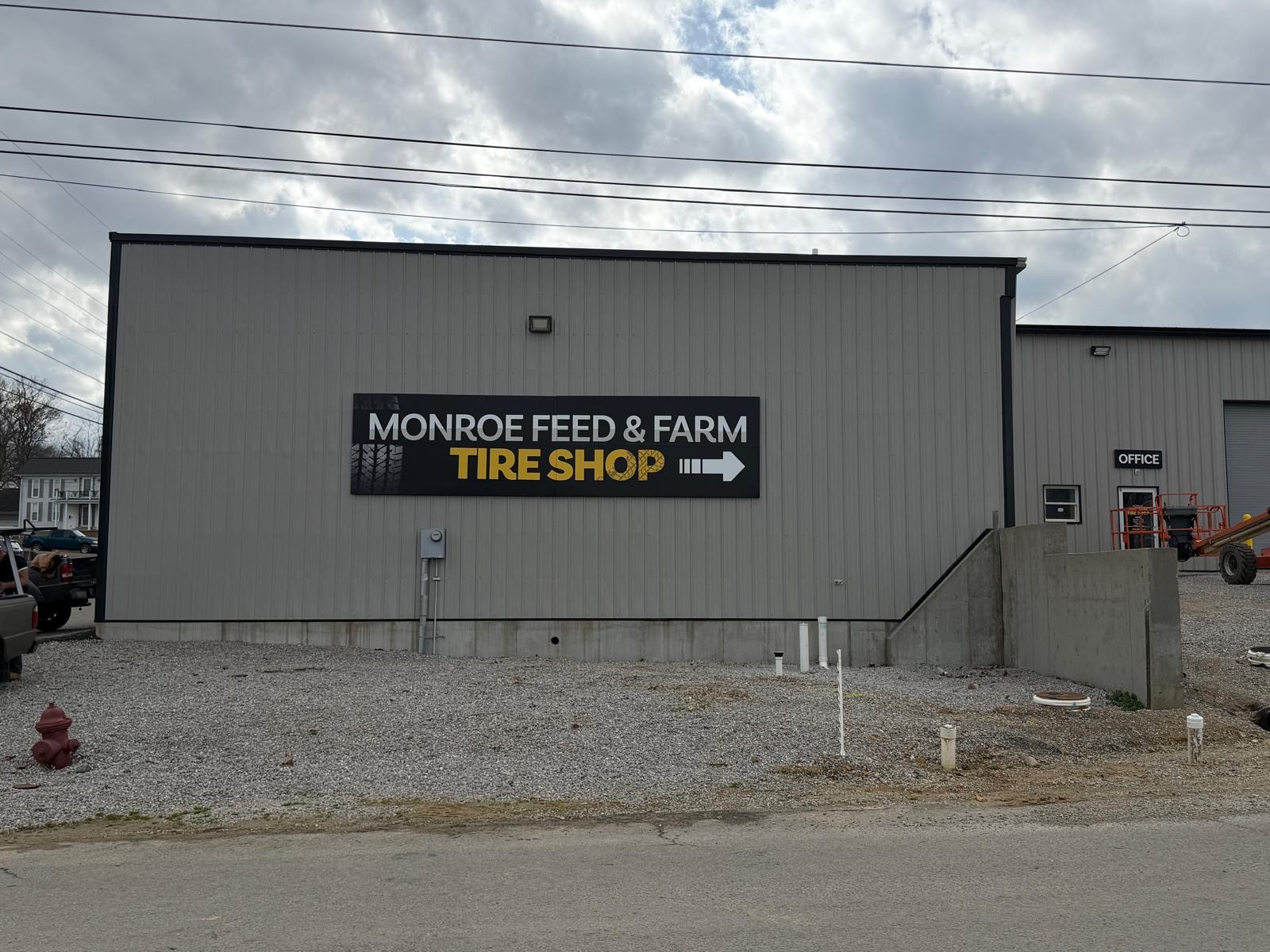 Large black ACM storefront sign reading Monroe Feed & Farm Tire Shop